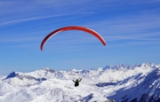 Image d'un parapente rouge au dessus des sommets enneigés